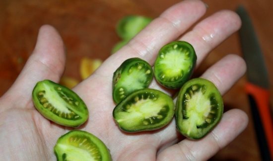 Разрезанные на половинки мелкие зелёные помидоры в руке человека
