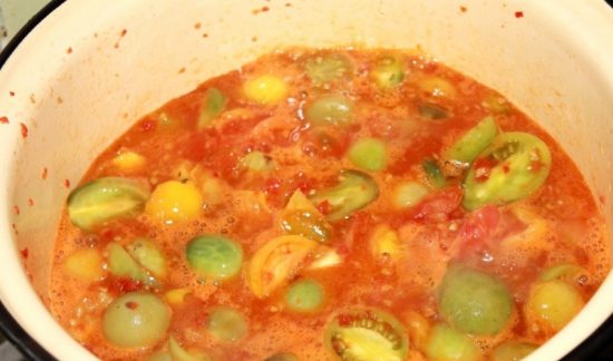 Кипящая заготовка из зелёных помидоров и других овощей в большой кастрюле