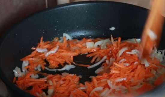 Обжарка моркови и репчатого лука в большой чёрной сковороде